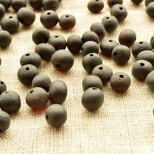 May include: A collection of dark brown wooden beads with a hole through the centre of each bead. The beads are scattered on a light brown fabric surface.