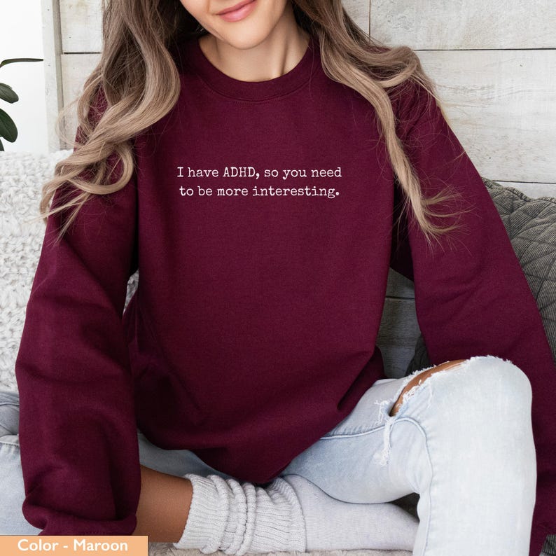 May include: Maroon sweatshirt with the text "I have ADHD, so you need to be more interesting." The sweatshirt is a solid color and has a crew neck.