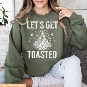 Op de afbeelding: Olijfgroene sweatshirt met de witte tekst "LET'S GET TOASTED". De afbeelding toont een kampvuur en marshmallows. Een comfortabele top, ideaal voor kamperen of buitenactiviteiten.