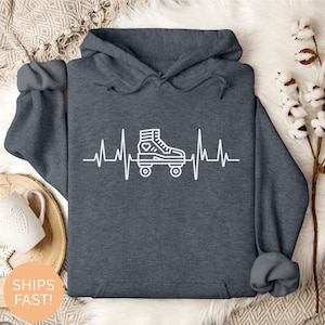 Puede incluir: Sudadera con capucha gris oscuro con un gráfico blanco de un patín en línea integrado en una línea de latido cardíaco. La sudadera tiene capucha y mangas largas. El diseño presenta un patín con un corazón.