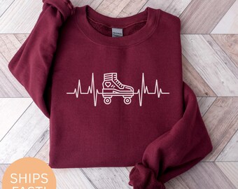 Könnte beinhalten: Ein weinrotes Sweatshirt mit einer weißen Grafik eines Rollschuhs, der in eine Herzschlaglinie integriert ist. Das Design beinhaltet ein Herz im Skate. Das Sweatshirt ist aus weichem Material.