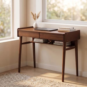 May include: A dark brown wooden desk featuring a flat rectangular top, two front drawers, and a lower open shelf. The desk has four tapered legs and is topped with a closed laptop, a stack of three books, and a white vase containing dried grass.