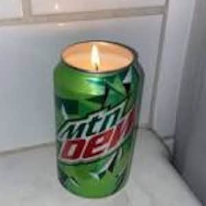 May include: A green and white can candle with the text "mtn dew" on the side. The candle is lit and the flame is visible.