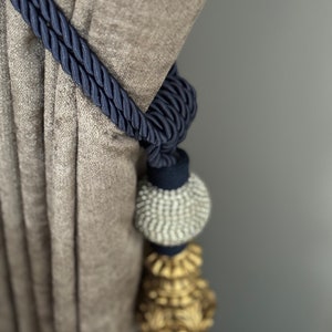 May include: A navy blue curtain tieback with a decorative tassel. The tassel features a silver bead and a gold-colored ornament.