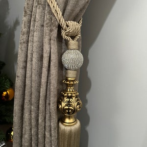 May include: A gold curtain tieback with a tassel and a decorative crystal ball. The tieback is made of a thick, braided rope.