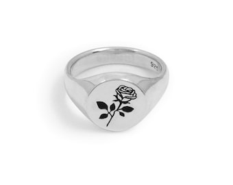 May include: A silver signet ring with a black rose design. The ring is engraved with the number 925.