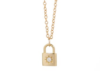 May include: A gold necklace with a small padlock pendant featuring a single diamond in the center. The padlock has a starburst design around the diamond.