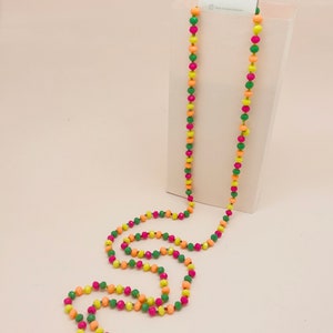 Peut inclure: Un long collier de perles multicolores avec des perles vertes, roses et orange. Le collier est sur un fond blanc avec une petite étiquette blanche qui dit "miracle".