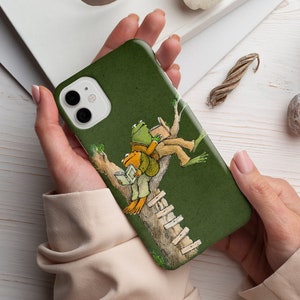 May include: A green phone case with a cartoon illustration of two frogs sitting on a tree branch and reading books. The frogs are green and brown with black eyes. The tree branch is brown with green leaves. The phone case is made of a soft, durable material.