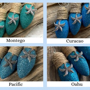 May include: Four teal blue lightbulb ornaments with silver starfish accents and brown twine. The ornaments are labeled "Montego", "Curacao", "Pacific", and "Oahu".