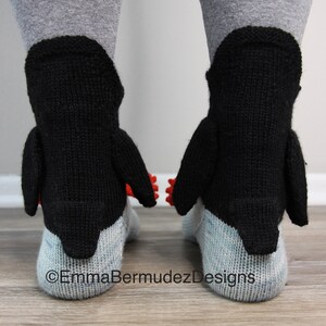 May include: A pair of black and white penguin socks with red accents. The socks are knitted and have a 3D penguin design.