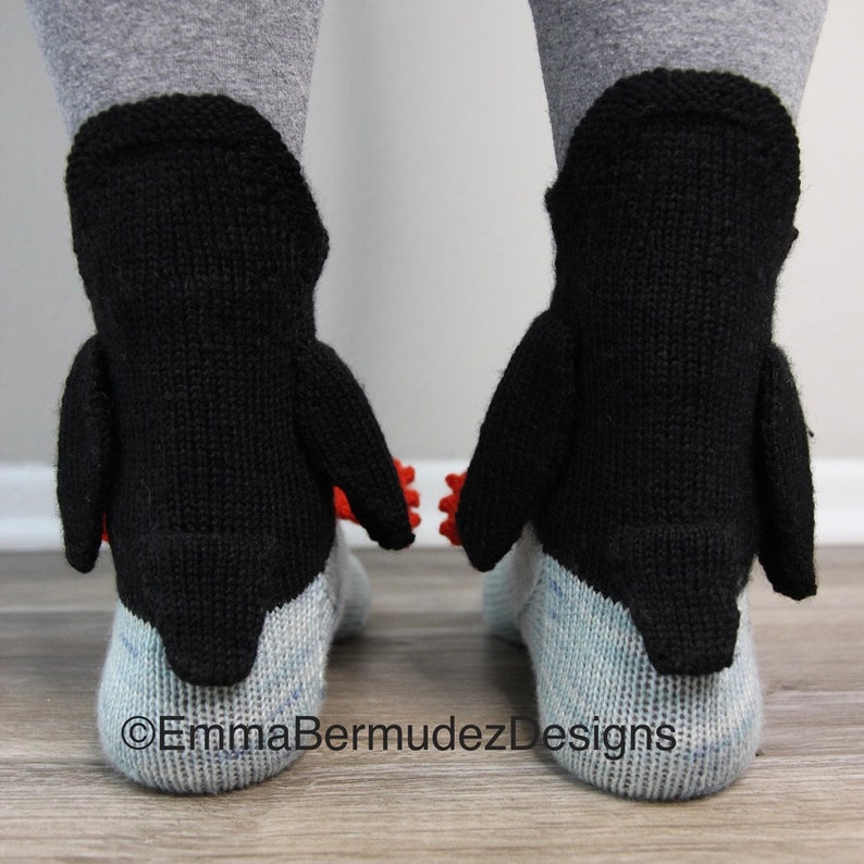 May include: A pair of black and white penguin socks with red accents. The socks are knitted and have a 3D penguin design.