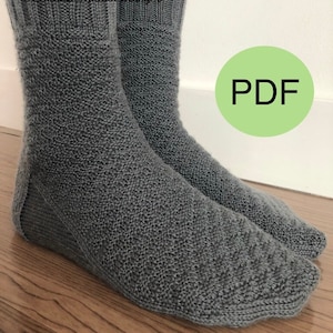 May include: A pair of gray knitted socks with a ribbed texture. The socks are shown on a wooden floor. The word "PDF" is written in black on a green circle.