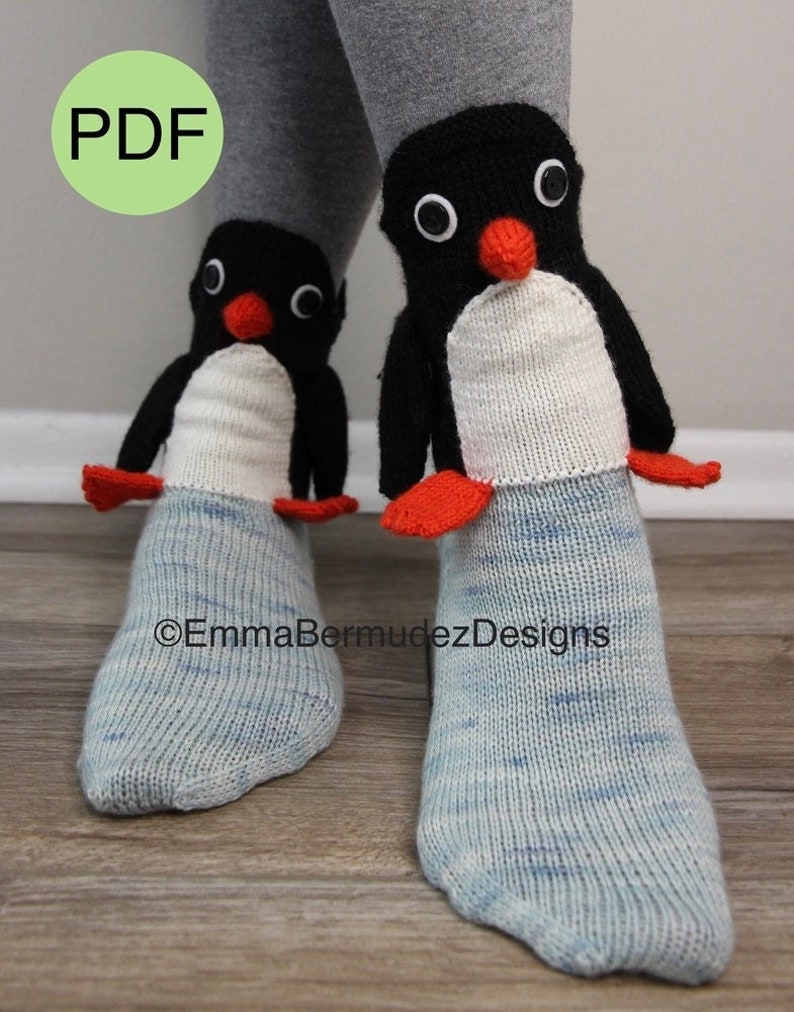 May include: A pair of blue and white knit socks with penguin-shaped cuffs. The penguins are black and white with red beaks and black eyes. The socks are on a wooden floor. The text "&copy;EmmaBermudezDesigns" is visible on the floor.