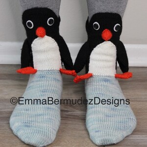 May include: A pair of blue and white knit socks with penguin faces on the top. The penguins have black bodies, white bellies, orange beaks, and black eyes.