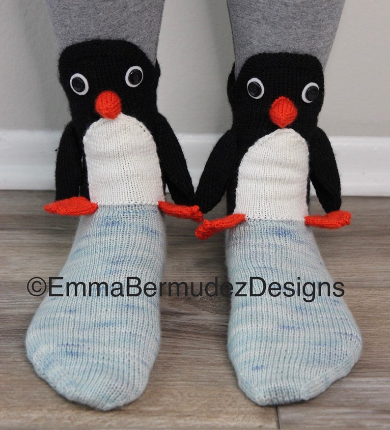 May include: A pair of blue and white knit socks with penguin faces on the top. The penguins have black bodies, white bellies, orange beaks, and black eyes.