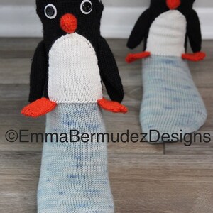 May include: A pair of blue and white knit socks with penguin appliques. The penguins have black bodies, white bellies, orange beaks, and black eyes.