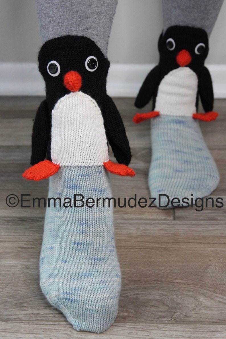 May include: A pair of blue and white knit socks with penguin appliques. The penguins have black bodies, white bellies, orange beaks, and black eyes.