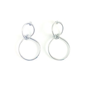 May include: A pair of silver hoop earrings with a knotted design. The earrings are made of thin metal and have a simple, modern look.