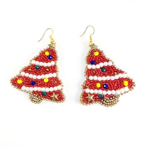 Op de afbeelding: Een paar rode, geperde kerstboom oorbellen met witte, gele, blauwe en groene accenten. De oorbellen zijn gemaakt van kleine kralen en hebben een gouden haak.