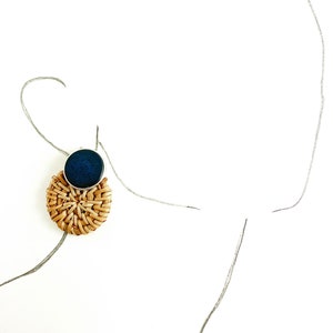 May include: A round woven wicker earring with a dark blue circular accent.