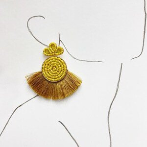Pode incluir: Um par de brincos de contas amarelas com franjas de borla. Os brincos são feitos com contas pequenas e redondas e têm um fecho de metal dourado.