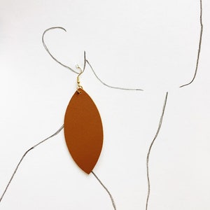 May include: A pair of brown leather earrings shaped like a leaf. The earrings have a gold hook.