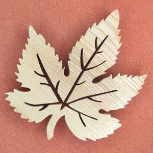 Peut inclure: Un dessous de verre en bois en forme de feuille avec un design détaillé. Le dessous de verre est brun clair et présente un grain de bois naturel.
