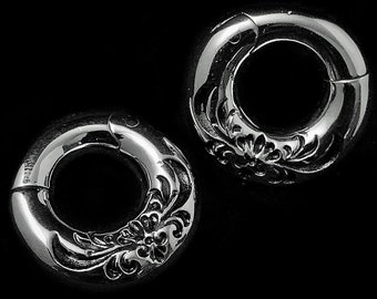 May include: A pair of circular silver-toned hoop earrings featuring a hinged closure mechanism. Each hoop is decorated with an embossed floral pattern that wraps around the outer surface, creating a textured design on the polished metallic finish.