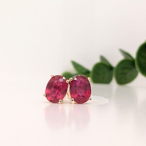 Op de afbeelding: Een paar ovale robijn oorbellen gezet in goud. De oorbellen zijn diep rood van kleur en hebben een gepolijste afwerking.