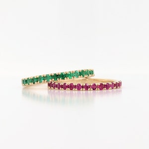 May include: Two gold eternity bands set with gemstones. One band is set with green emeralds and the other with pink rubies.
