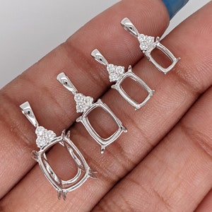 May include: Four silver pendant settings with a bezel setting and a row of small clear stones at the top. The settings are different sizes and are held in a hand.