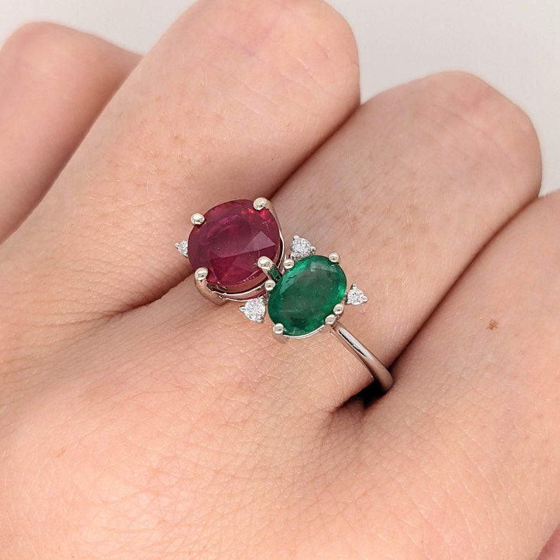 Op de afbeelding: Een ring van witgoud met een rode robijn en een groene smaragd. De ring is bezet met kleine diamanten.