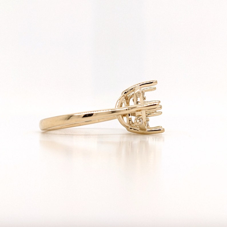 Op de afbeelding: Een gouden ringbezetting met een delicaat, ingewikkeld ontwerp. De bezetting heeft een centrale kraalbezetting voor een grote steen, omringd door kleinere kraalbezettingen voor accentstenen.