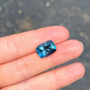 May include: A deep blue gemstone with a cushion cut, displayed on a finger.