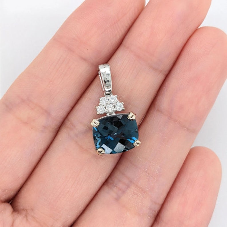 May include: A pendant featuring a large, cushion-cut, deep blue topaz gemstone surrounded by a halo of smaller, round, white diamonds. The pendant is crafted in silver and has a bail for attaching to a chain.