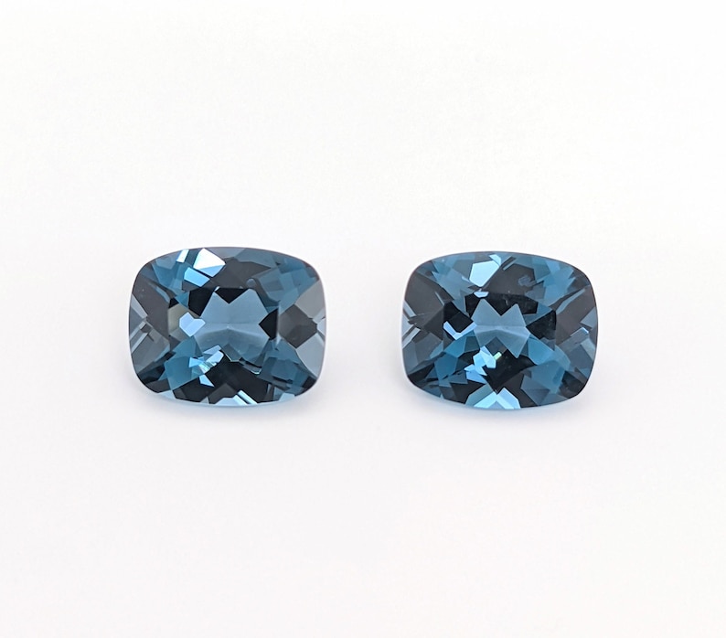 May include: Two cushion-cut blue topaz gemstones, each with a slightly different shade of blue.