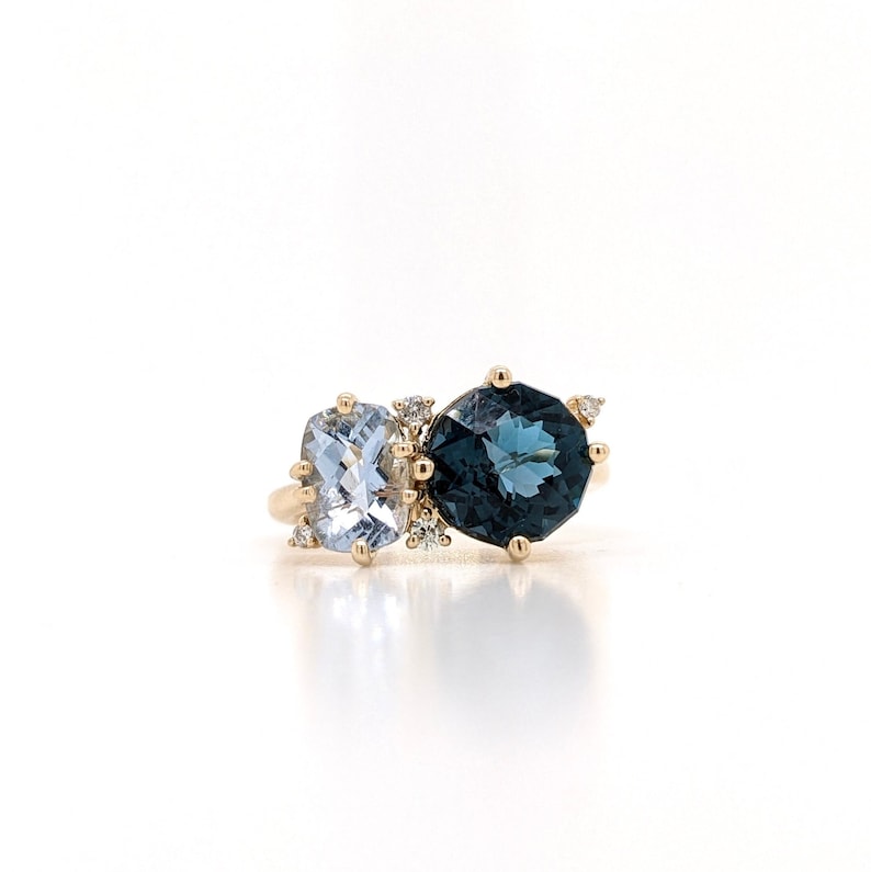 Op de afbeelding: Een gouden ring met een blauwe en een lichtblauwe edelsteen. De ring is bezet met kleine diamanten.