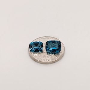 May include: Two blue topaz gemstones, one slightly larger than the other, are displayed on a US quarter. The smaller stone measures 8x6mm and the larger stone measures 9x7mm.