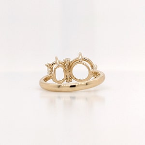 Op de afbeelding: Een gouden ring met twee ovale settings voor edelstenen. De ring is versierd met kleine diamanten.