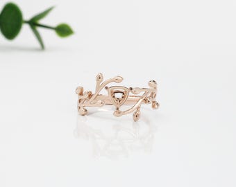 May include: A delicate rose gold ring with a triangular shaped setting and a vine design. The ring is set on a white background.