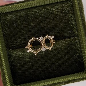 Op de afbeelding: Een gouden ringbezetting met twee ovale openingen voor edelstenen. De bezetting is versierd met kleine diamanten rond de randen.