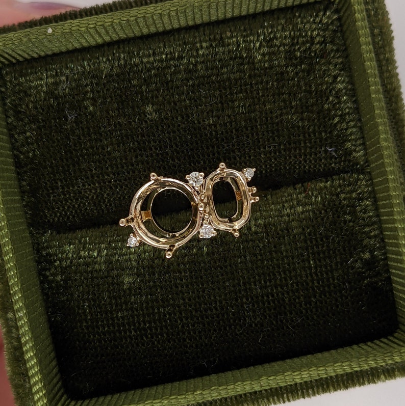 Op de afbeelding: Een gouden ringbezetting met twee ovale openingen voor edelstenen. De bezetting is versierd met kleine diamanten rond de randen.