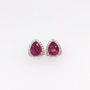 May include: A pair of ruby and diamond earrings. The earrings are set in a triangular shape with a pear-shaped ruby in the centre and a halo of diamonds around it.