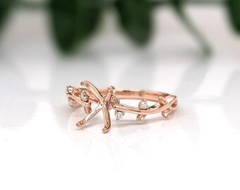 May include: Rose gold engagement ring with a floral vine design. The ring features a prong setting for a center stone and is adorned with small, sparkling accent stones. The band is shaped like delicate vines with leaves.