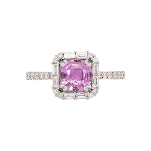 May include: A silver ring featuring a large, square-cut pink gemstone surrounded by a halo of smaller, clear gemstones. The ring's band is also adorned with small, clear gemstones, creating a sparkling and elegant design.
