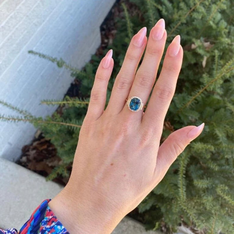 May include: A gold ring featuring a large, cushion-cut blue topaz gemstone encircled by a halo of smaller diamonds.