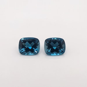 May include: Two cushion-cut, deep blue topaz gemstones. The gemstones are faceted and have a brilliant shine.