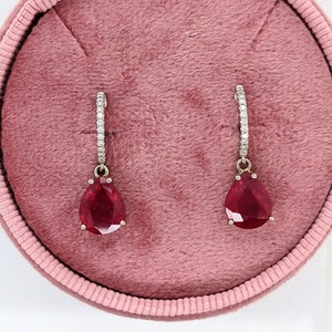May include: A pair of pear-shaped ruby earrings with diamond halo settings. The earrings are suspended from a diamond-encrusted hoop.