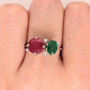 Op de afbeelding: Een zilveren ring met een rode robijn en een groene smaragd. De ring is bezet met kleine diamanten.
